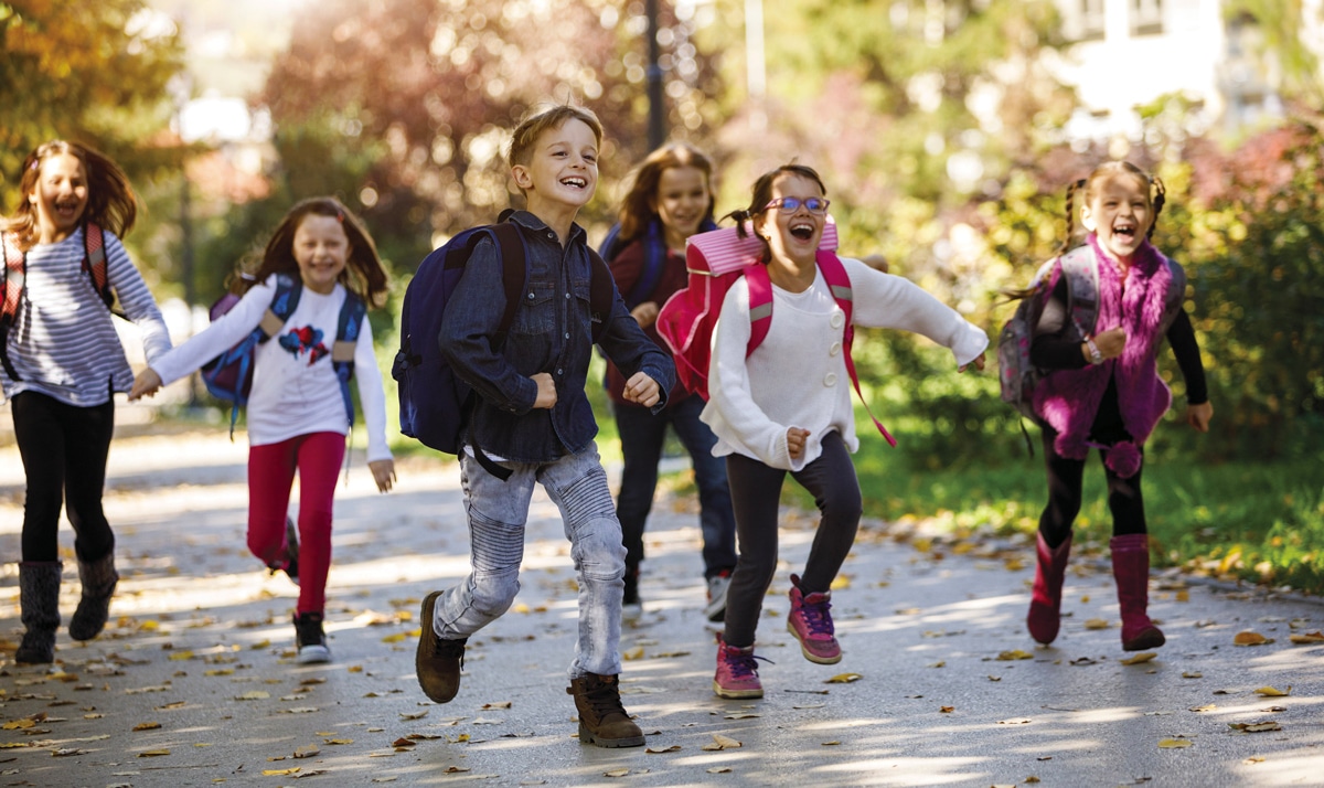 A group of young kids running along a path with backpacks.