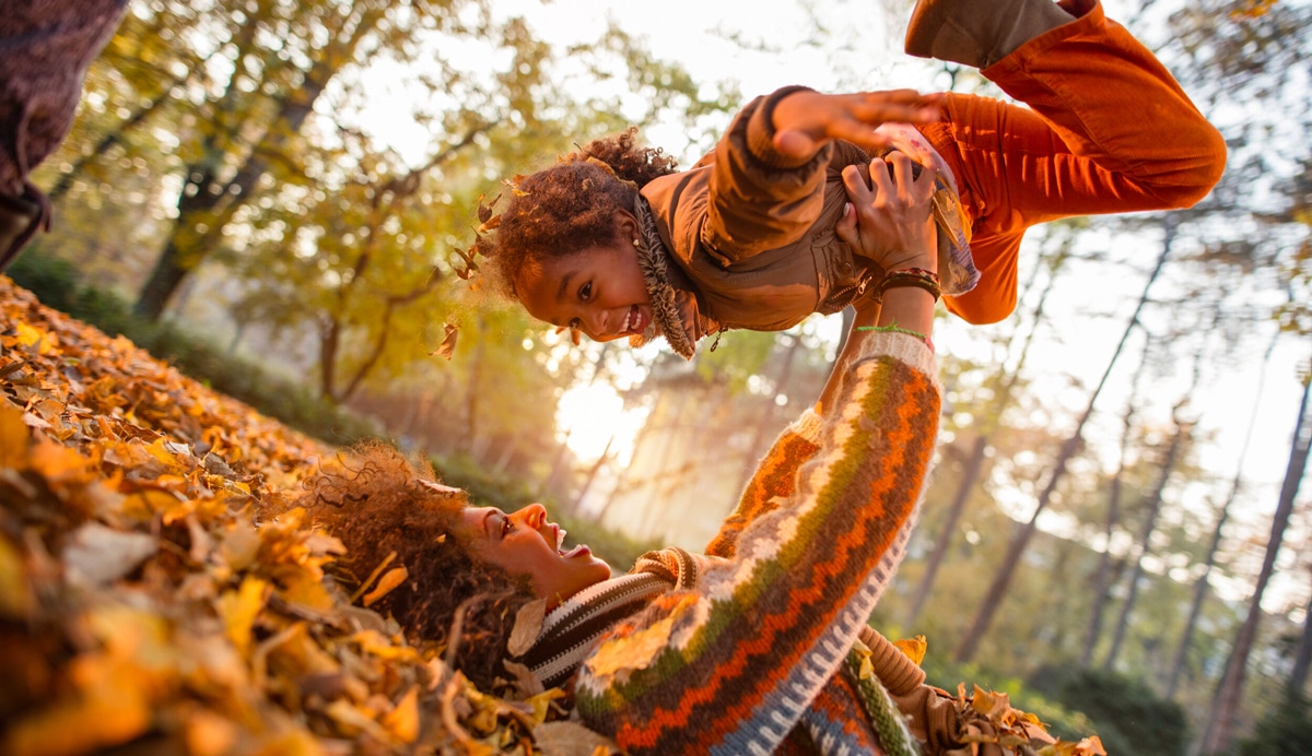 A mother and daughter playing in the leaves during Autumn.