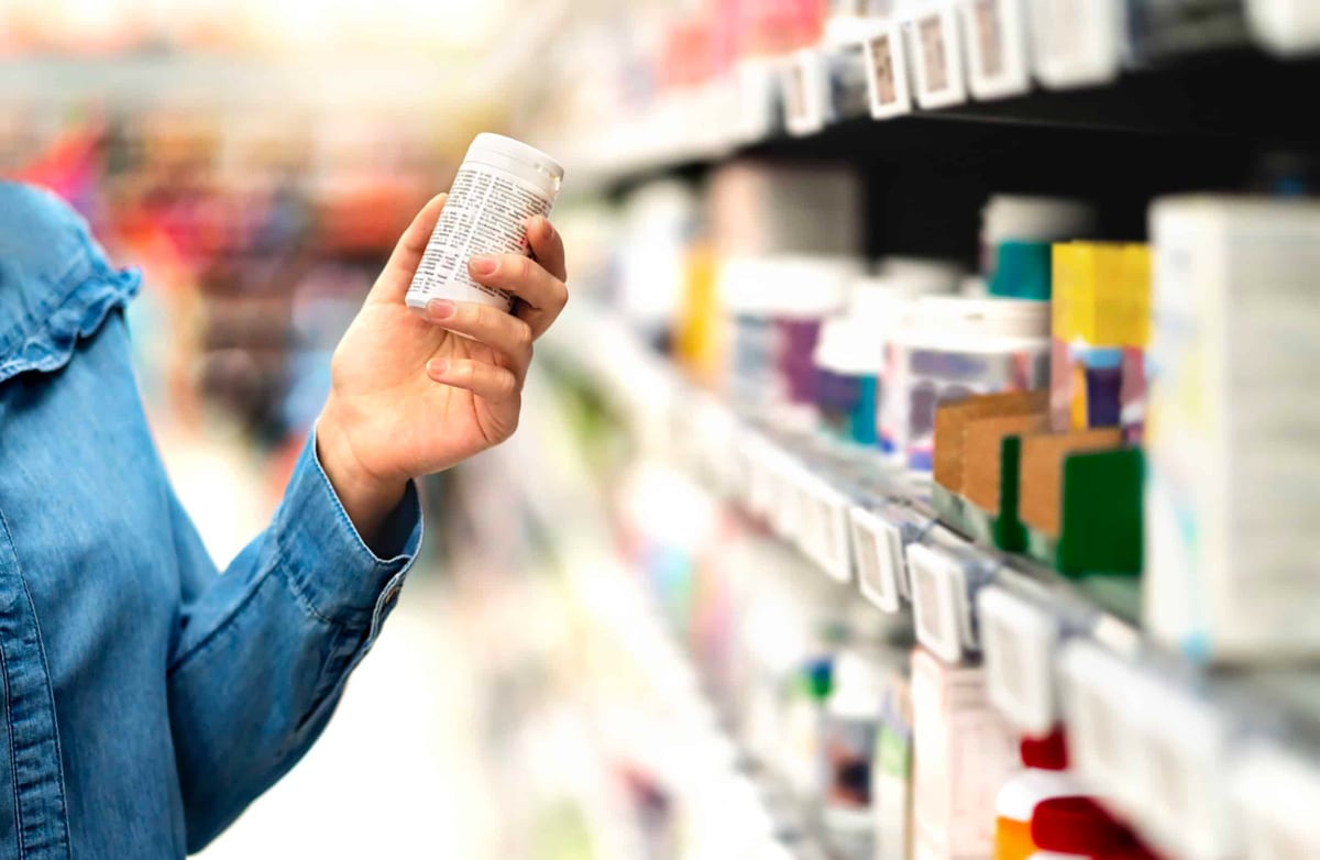 A close up shot of someone's hand removing a bottle of medication from a shelf.