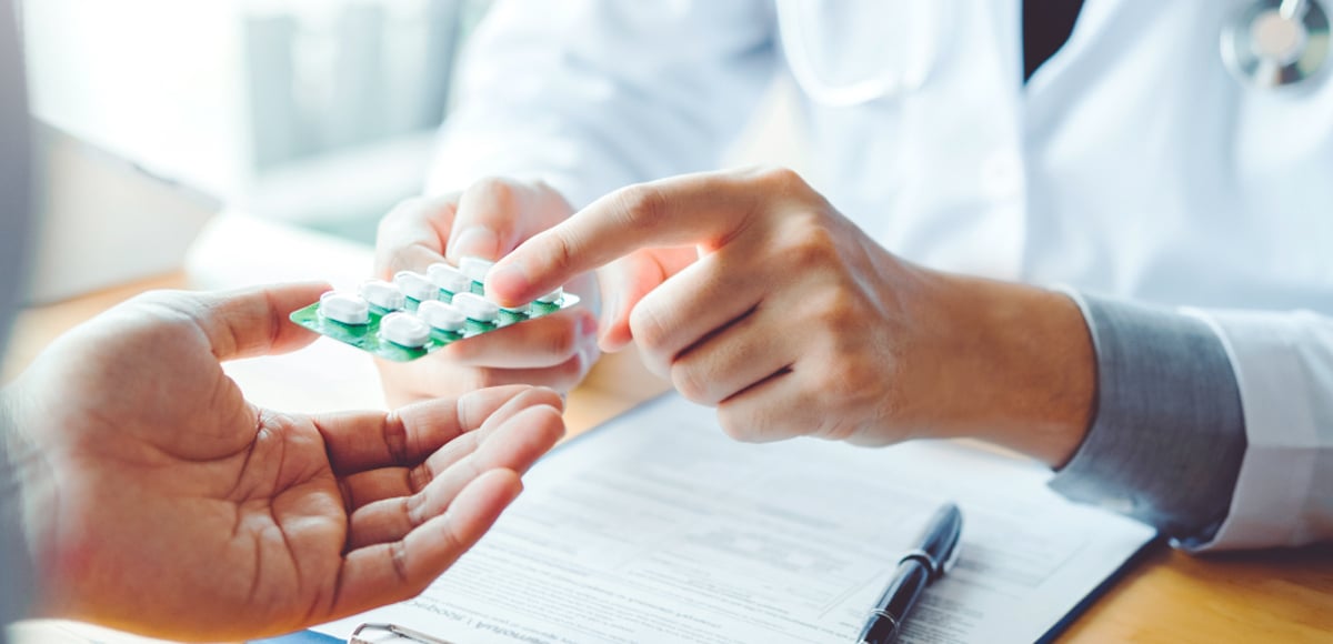 A close up image of a pharmacist handing a packet of pills to a patient.