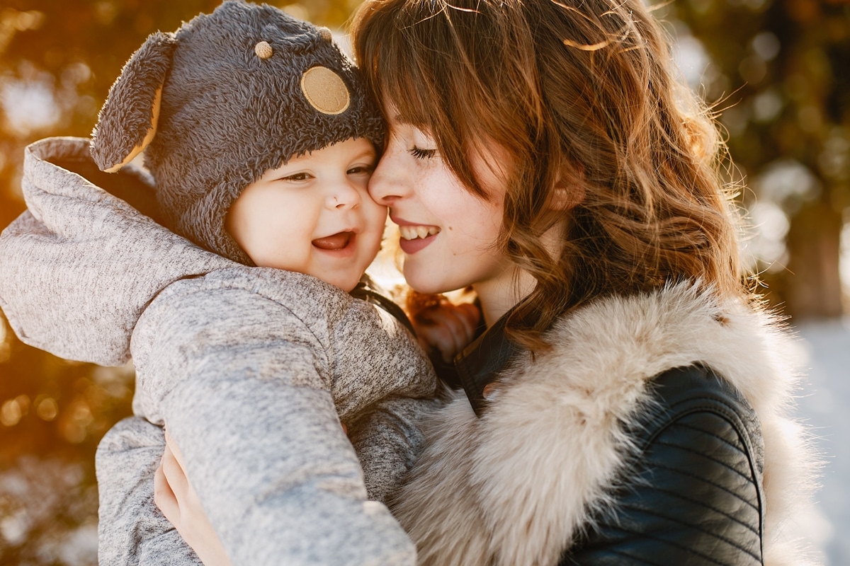 A mother holding their child outdoors on a winter day.